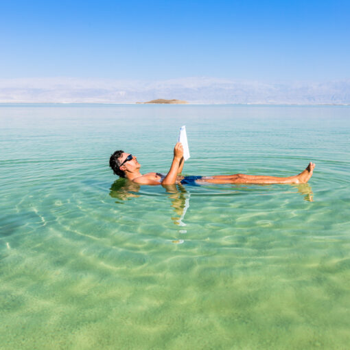 Ein Mann Ließt Zeitung während er auf der Wasseroberfläche des Toten Meeres liegt