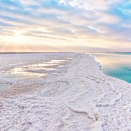 Die Morgensonne scheint auf eine Küste aus Salzkristallen auf der linken Seite vom Bild . Klares stilles Türkis Farben es Wasser auf der Rechten Seite des Bildes